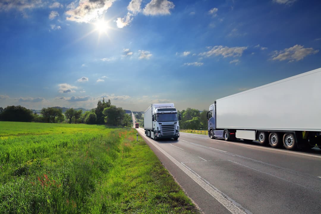 Twee vrachtwagen tegenliggers met groen landschap en blauwe hemel met zon